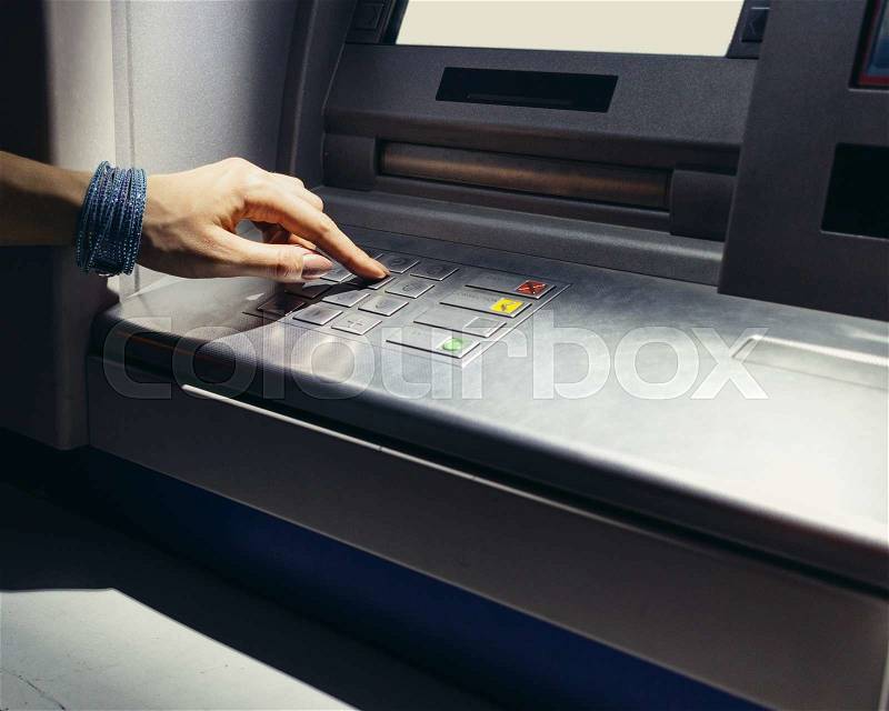 Female hand entering the secret code in the ATM at night on the street, stock photo