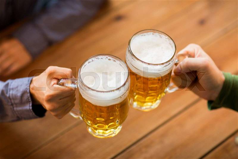 People, leisure and drinks concept - close up of male hands clinking beer mugs at bar or pub, stock photo