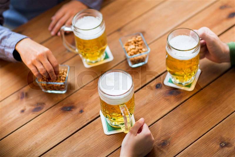 People, leisure and drinks concept - close up of male hands with beer mugs and peanuts at bar or pub, stock photo