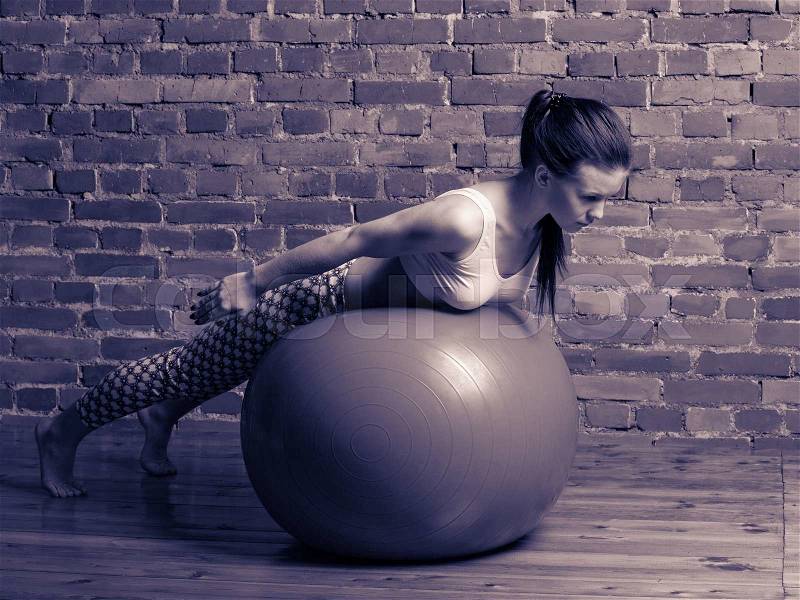 Fitness. Young brunette woman performing hyperextensions on the fitball at the gym, stock photo