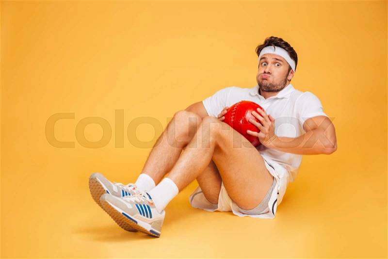 Funny sports man working out with fitness ball isolated on a orange background, stock photo