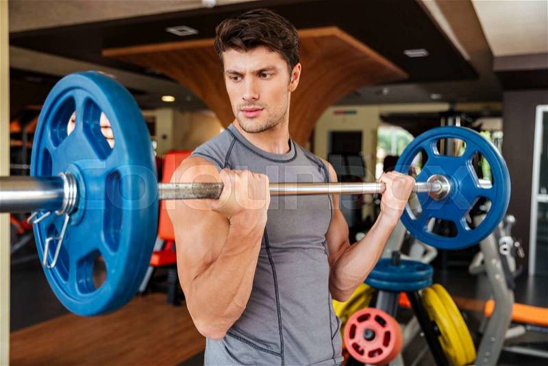 Handsome young man athlete working out with barbell in gym, stock photo