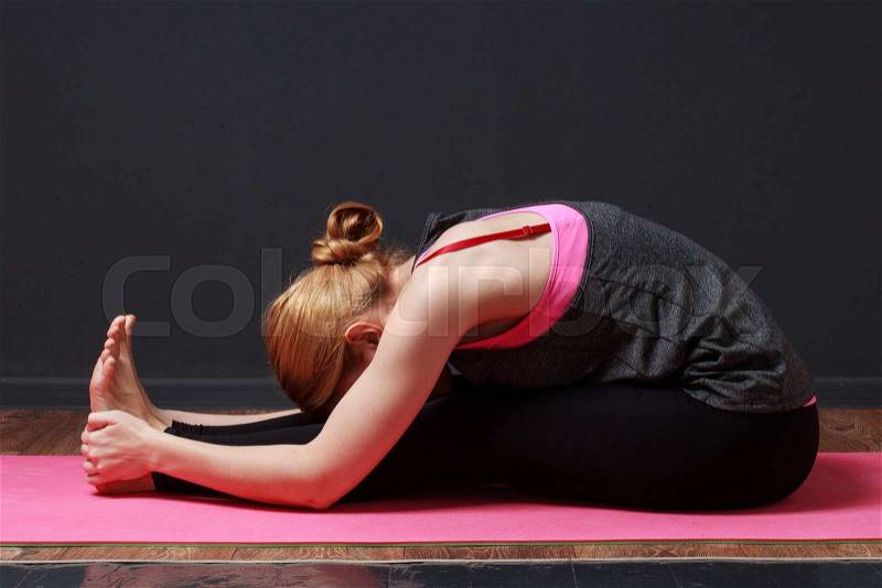 Seated forward fold. Young blonde woman doing yoga exercise, stock photo