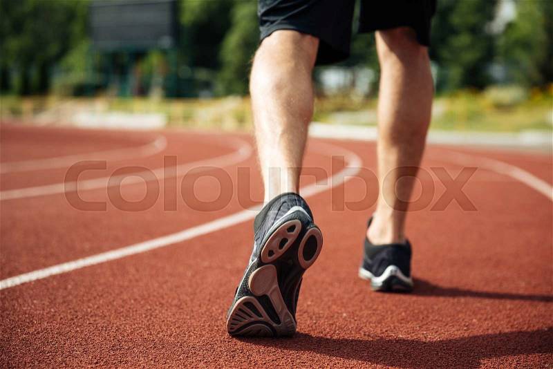Legs of young sportsman running on stadium track, stock photo