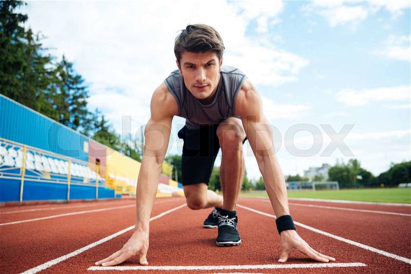 Young concentrated male athlete about to start a sprint and looking at camera, stock photo