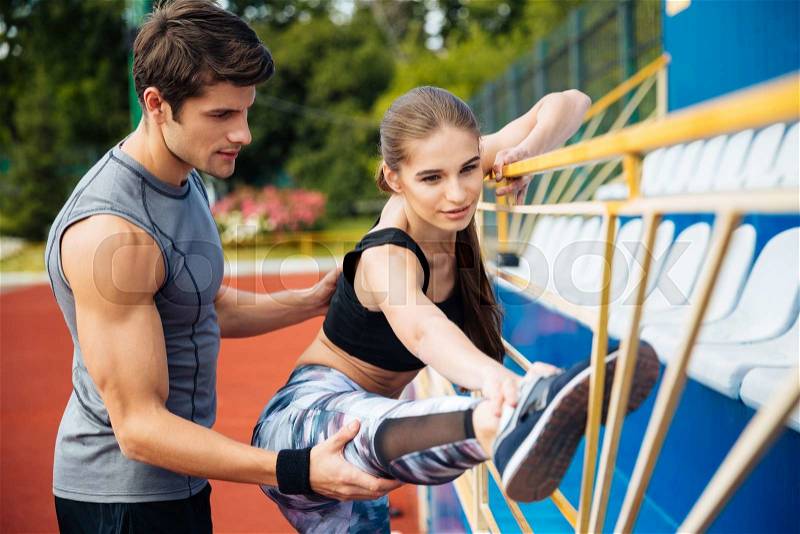 Cute young woman athlete working out with personal trainer on stadium, stock photo