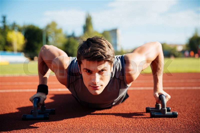 Young male athlete makes push ups on a racetrack at the stadium, stock photo