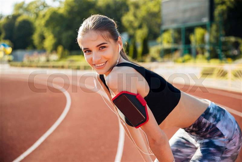 Young smiling cheerful female athlete ready to start running at the stadium track, stock photo