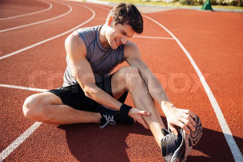 Young male runner suffering from leg cramp on the track at the stadium, stock photo
