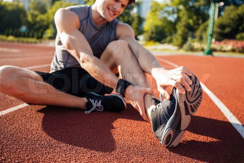 Cropped image of a runner suffering from leg cramp at the stadium, stock photo