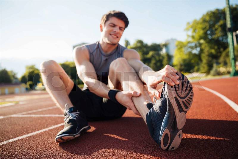 Young male runner suffering from leg cramp on the track at the stadium, stock photo