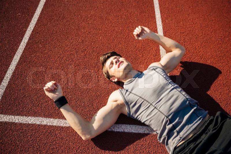 Fitness young man laying on running track after hard workout at the stadium, stock photo