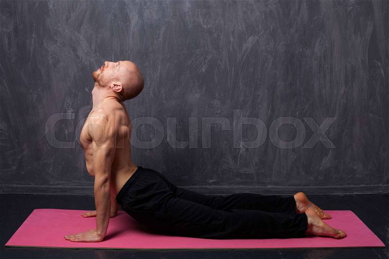 Man doing stretching. A man with a naked torso doing yoga cobra on underground background, stock photo