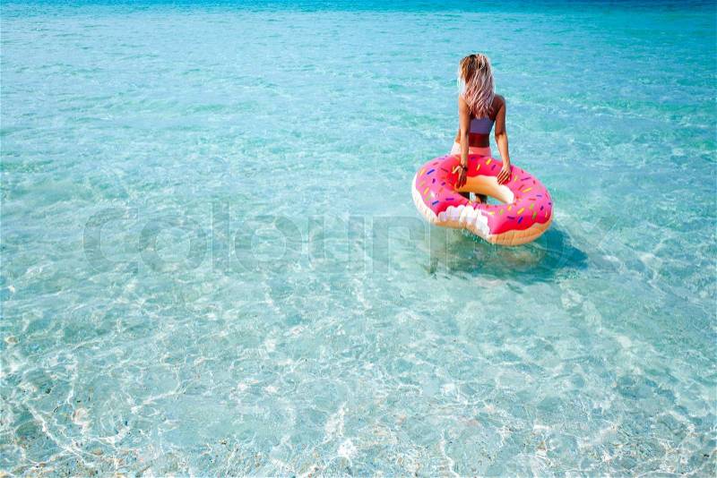 Woman swimming with inflatable donut on the beach in summer sunny day, stock photo