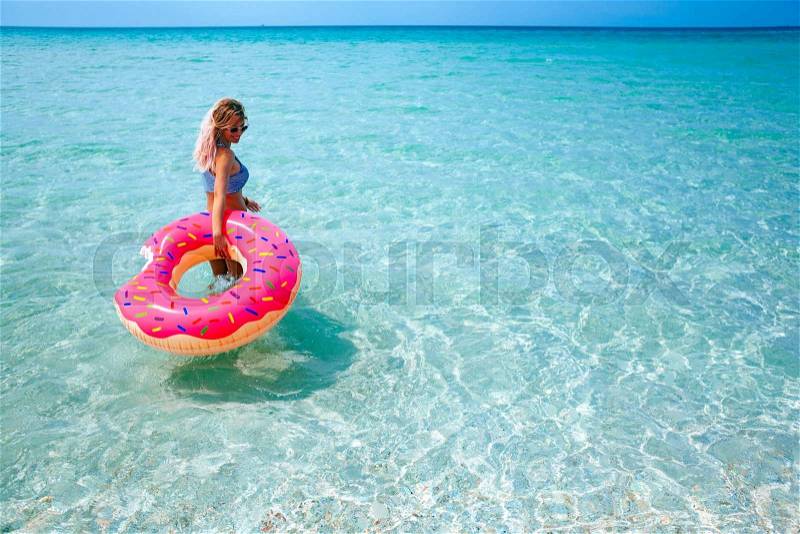 Woman swimming with inflatable donut on the beach in summer sunny day, stock photo