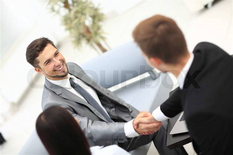 Two happy young men shaking hands while sitting at the office, stock photo