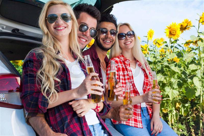 Friends drinking beer bottles sitting in car trunk outdoor countryside, happy smile people group summer sunflower field, stock photo