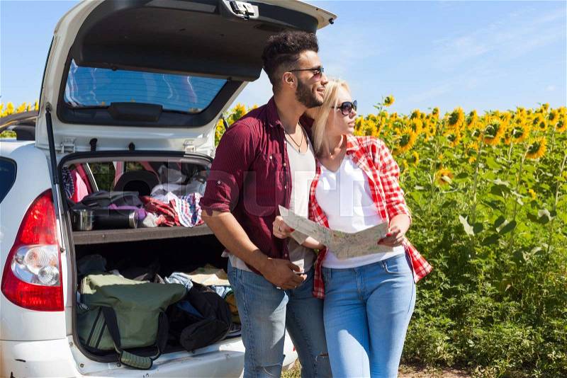 Couple looking road map standing sunflowers field outdoor, mix race man and woman standing near car trunk summer day holiday trip, stock photo