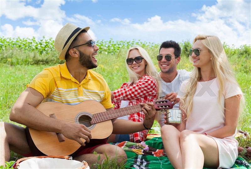Young people listening guy playing guitar group friends summer day sitting green grass outdoor picnic nature two couple men with girls laugh singing song together, stock photo