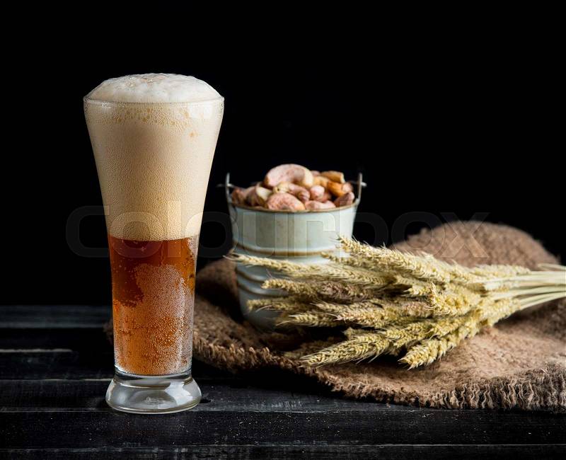 Tall beer glass with dark beer and wheat on black wood, stock photo