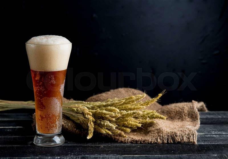 Tall beer glass with dark beer and wheat on black wood, stock photo