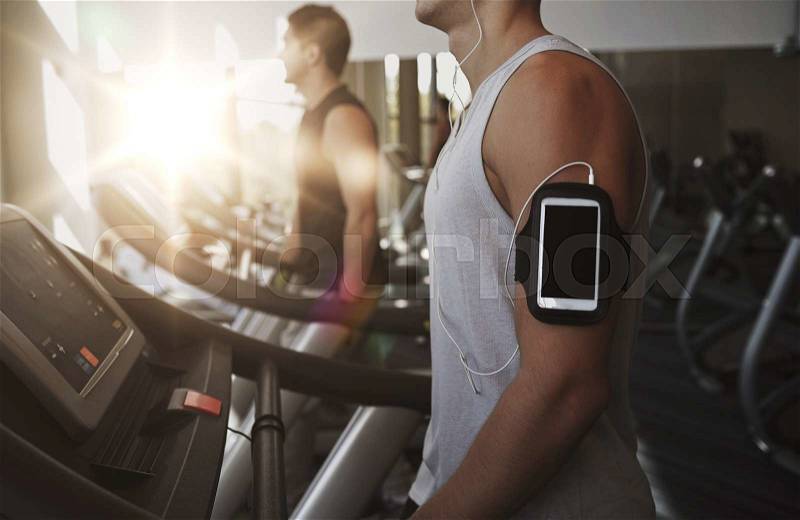 Sport, fitness, lifestyle, technology and people concept - man with smartphone and earphones exercising and listening to music on treadmill in gym, stock photo