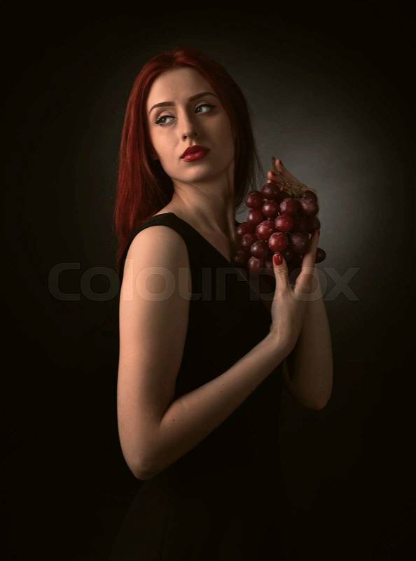 Beautiful redheaded woman in a black dress with grape, stock photo