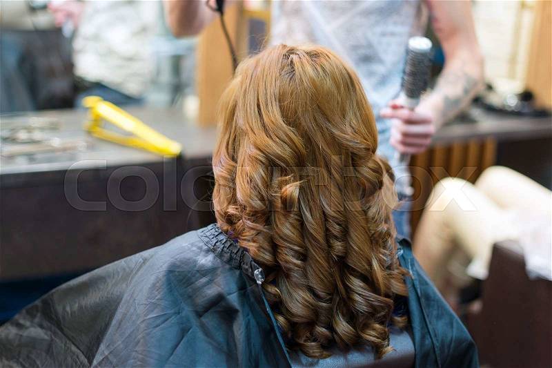 Professional hairdresser using curling iron. Hair curls in salon, people at work, stock photo