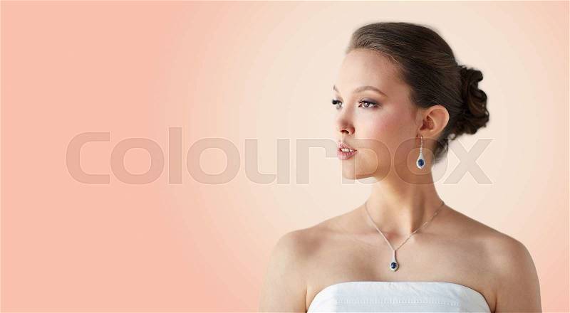 Beauty, jewelry, wedding accessories, people and luxury concept - beautiful asian woman or bride with earring and pendant over beige background, stock photo