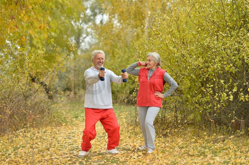 Happy fit senior couple exercising in autumn park, stock photo