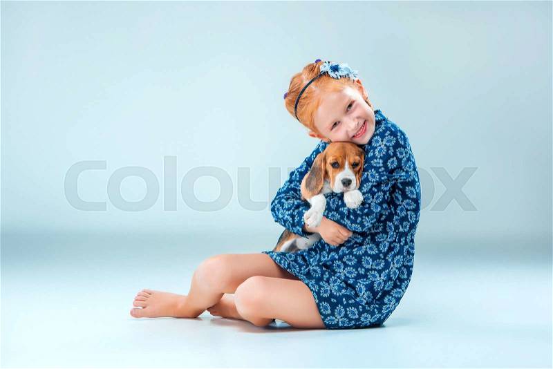 The happy girl and a beagle puppie on gray background, stock photo