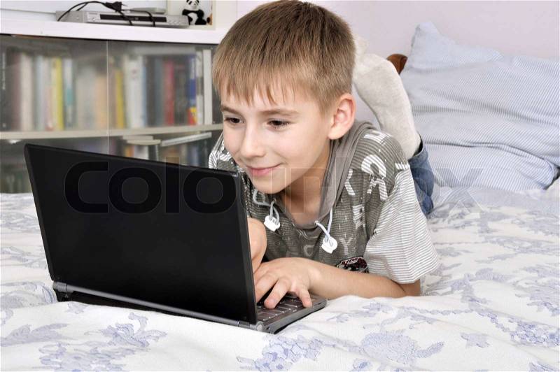 Happy little boy with laptop lying on the bad at home - indoors, stock photo