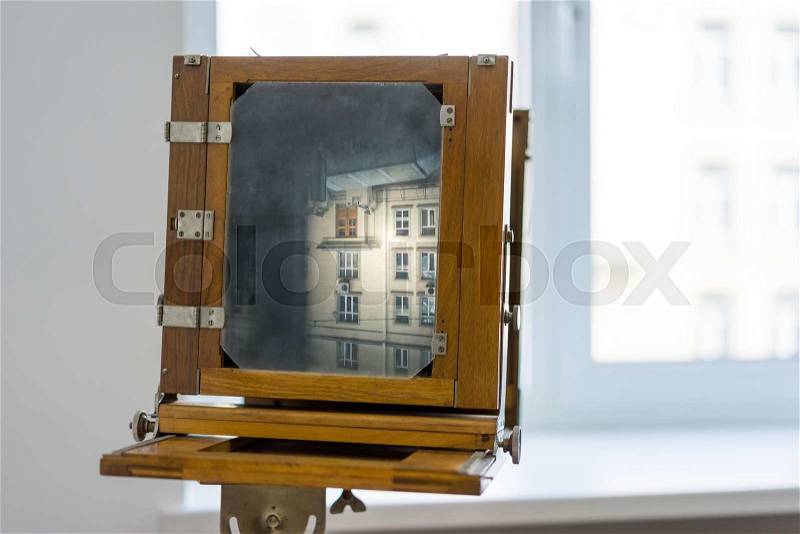 Vintage box camera with a wooden body standing near the window on white background, stock photo