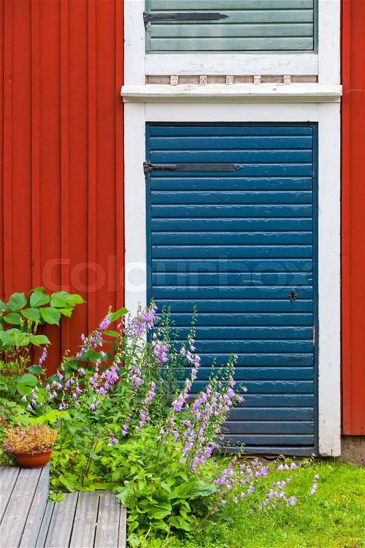 Porvoo, Finland. Old traditional Finnish architecture fragment. Decorative flowers near red blue closed door in red wooden wall, stock photo