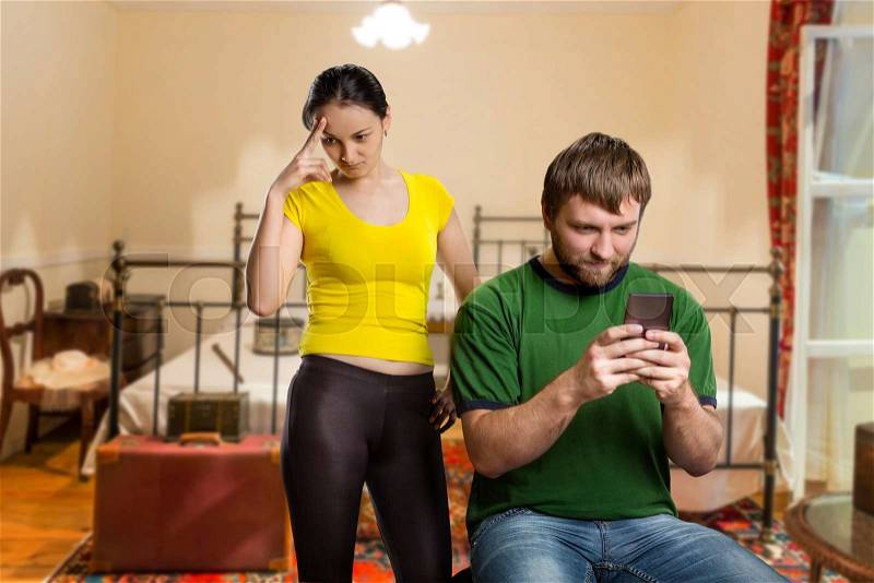 Adult man playing with his phone, wife in angry in the room, stock photo