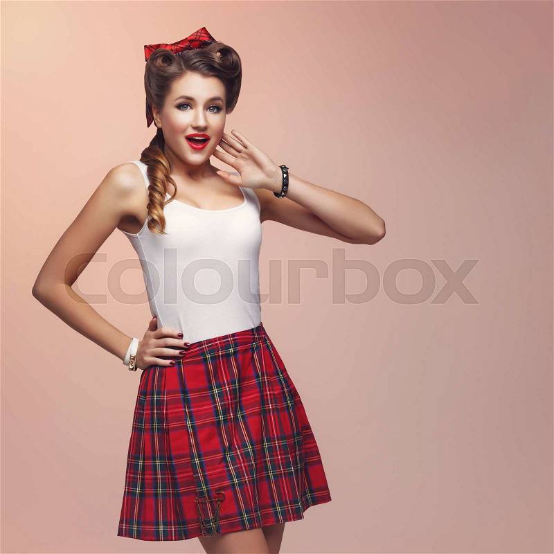 Beautiful young woman dressed in pin up style with retro makeup and hairstyle. Expression. Studio shot over beige background, stock photo