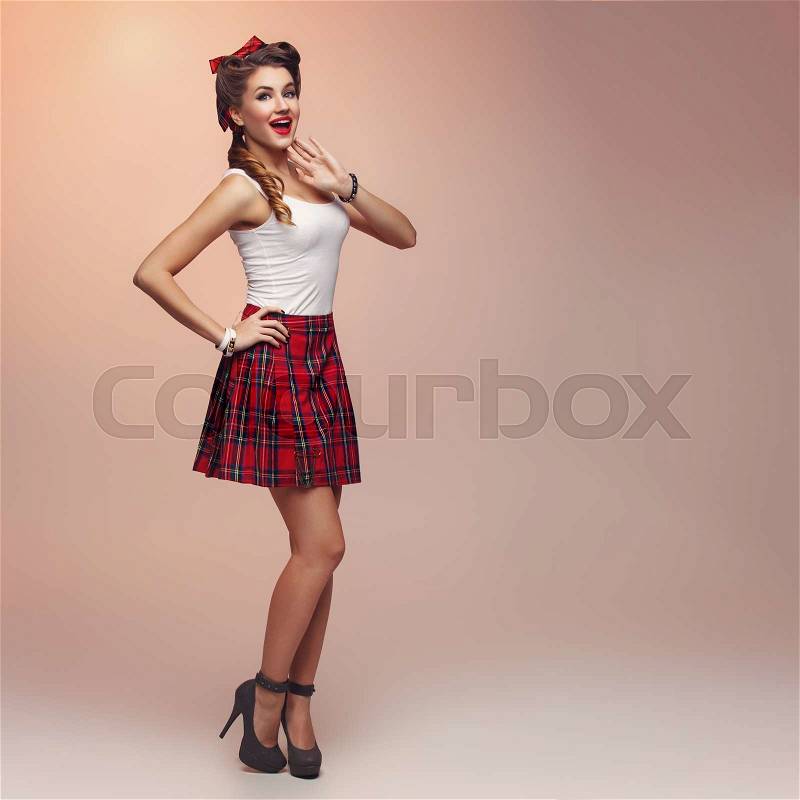 Beautiful young woman dressed in pin up style with retro makeup and hairstyle standing. Full body studio shot over beige background, stock photo