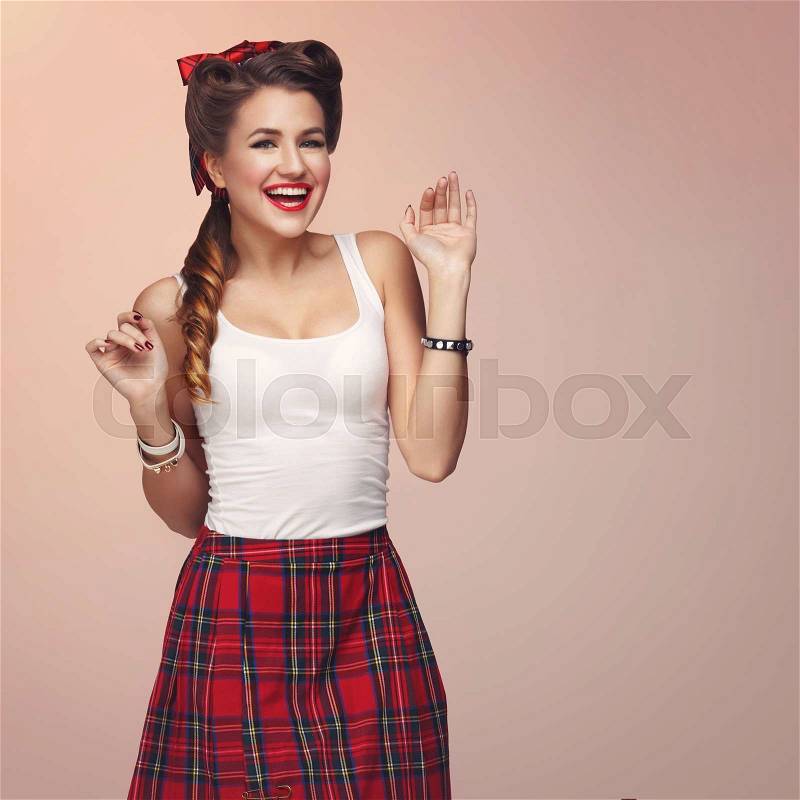Beautiful young woman dressed in pin up style with retro makeup and hairstyle. Expression. Studio shot over beige background, stock photo
