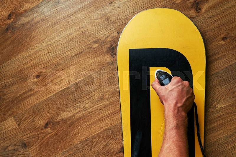 Man ironed wax on a snowboard, lying on the wooden floor, stock photo