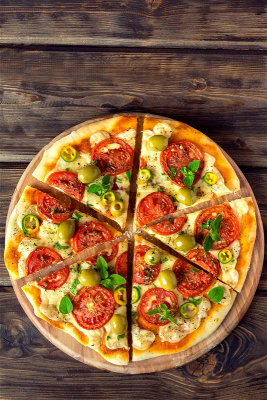 Homemade vegetable pizza with tomatoes, green olives, pepper, basil, oregano and cheese on wooden table with copy space, stock photo
