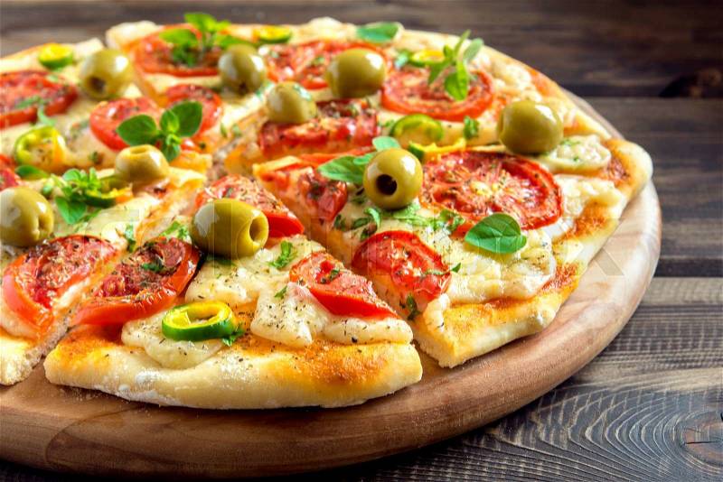 Homemade vegetable pizza with tomatoes, green olives, pepper, basil, oregano and cheese on wooden table with copy space, stock photo