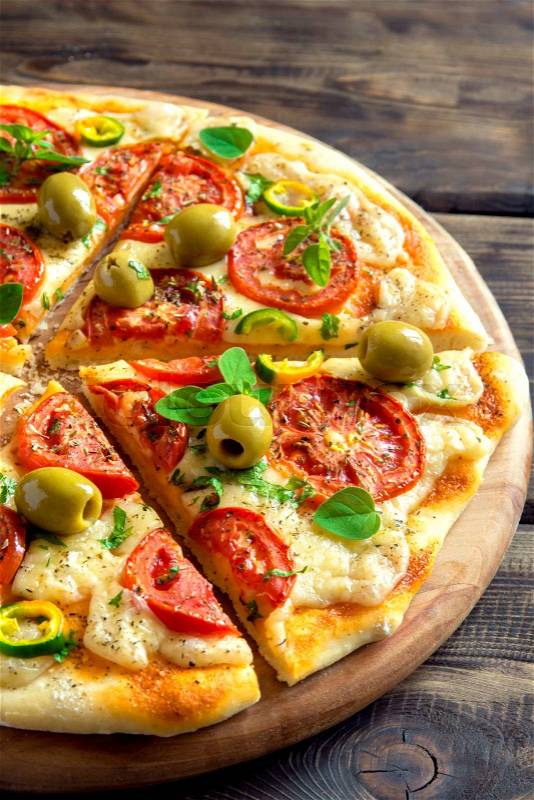 Homemade vegetable pizza with tomatoes, green olives, pepper, basil, oregano and cheese on wooden table close up, stock photo