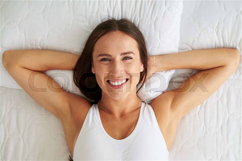 Beautiful young woman lying while holding hands behind head and lying in the bed, stock photo