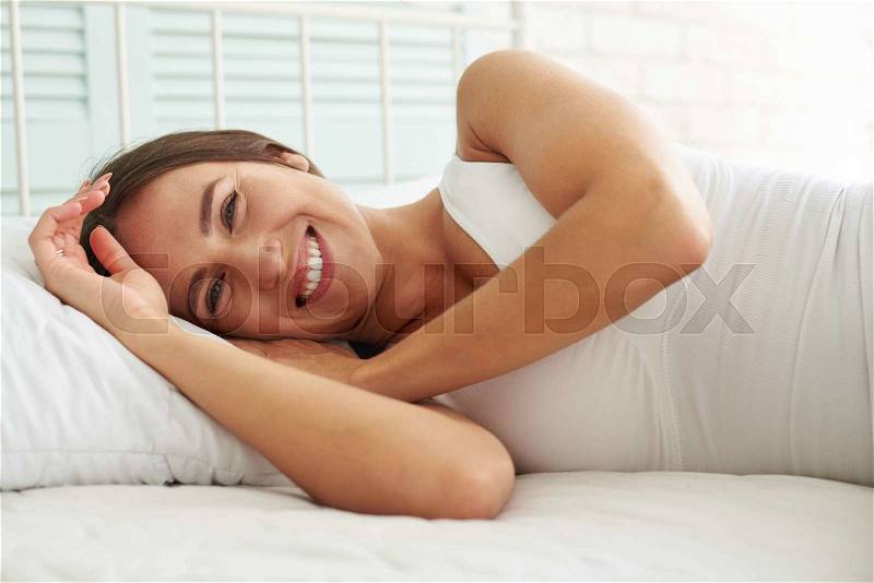 She looks happy and at ease while lying early on the bed , stock photo