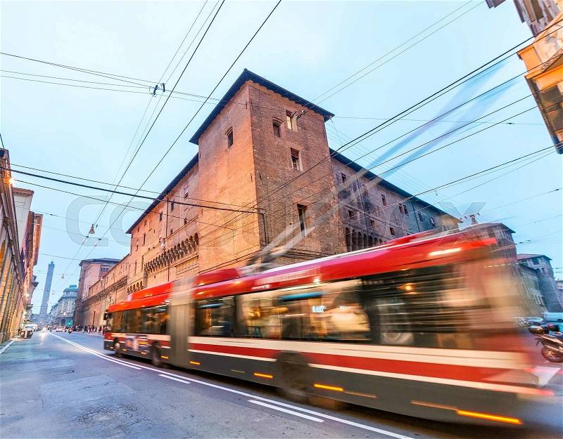 Red bus speeding up in Bologna streets at dusk, stock photo