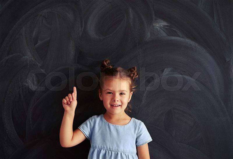 Small princess in a light-blue dress with a cute haircut showing finger on the top, stock photo