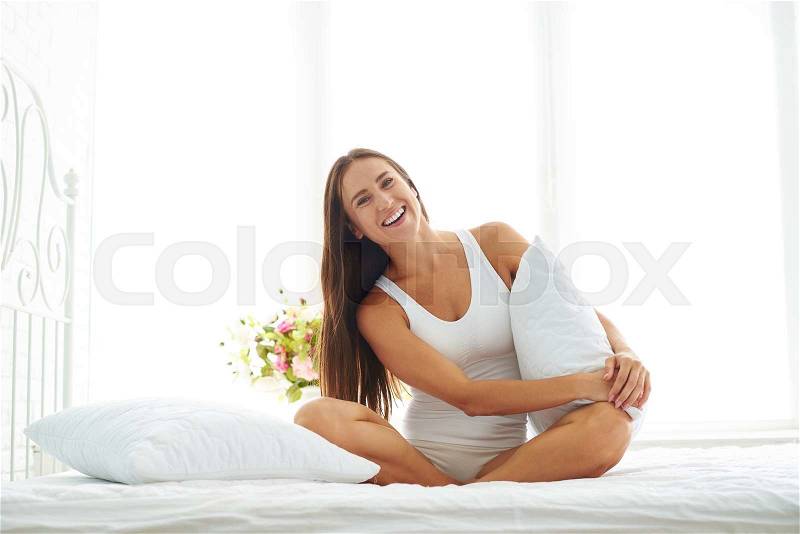 Young girl in a white nightgown basking in the peaceful atmosphere. She looks calm, happy and relaxed in the bedroom early in the morning, stock photo