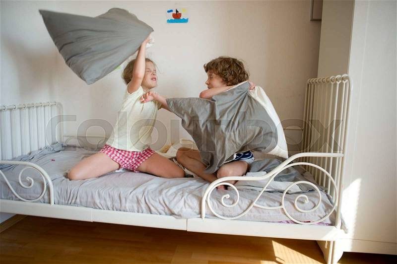 Little brother and sister staged a pillow fight on the bed in the bedroom. Naughty children beat each other pillows. They like that kind of game, stock photo
