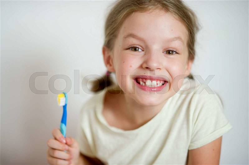 Funny girl with pigtails brushing his teeth. She shows their clean white teeth with a cheerful smile, stock photo