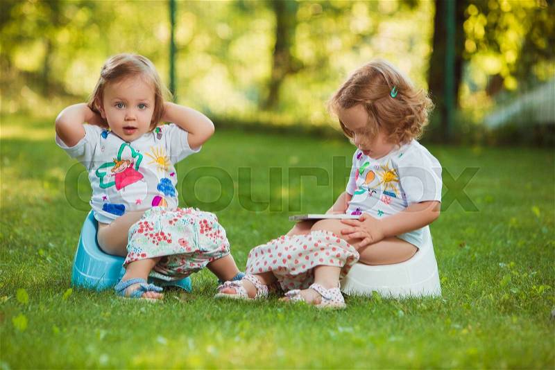 The two little baby girls two-year old sitting on pots against green grass, stock photo